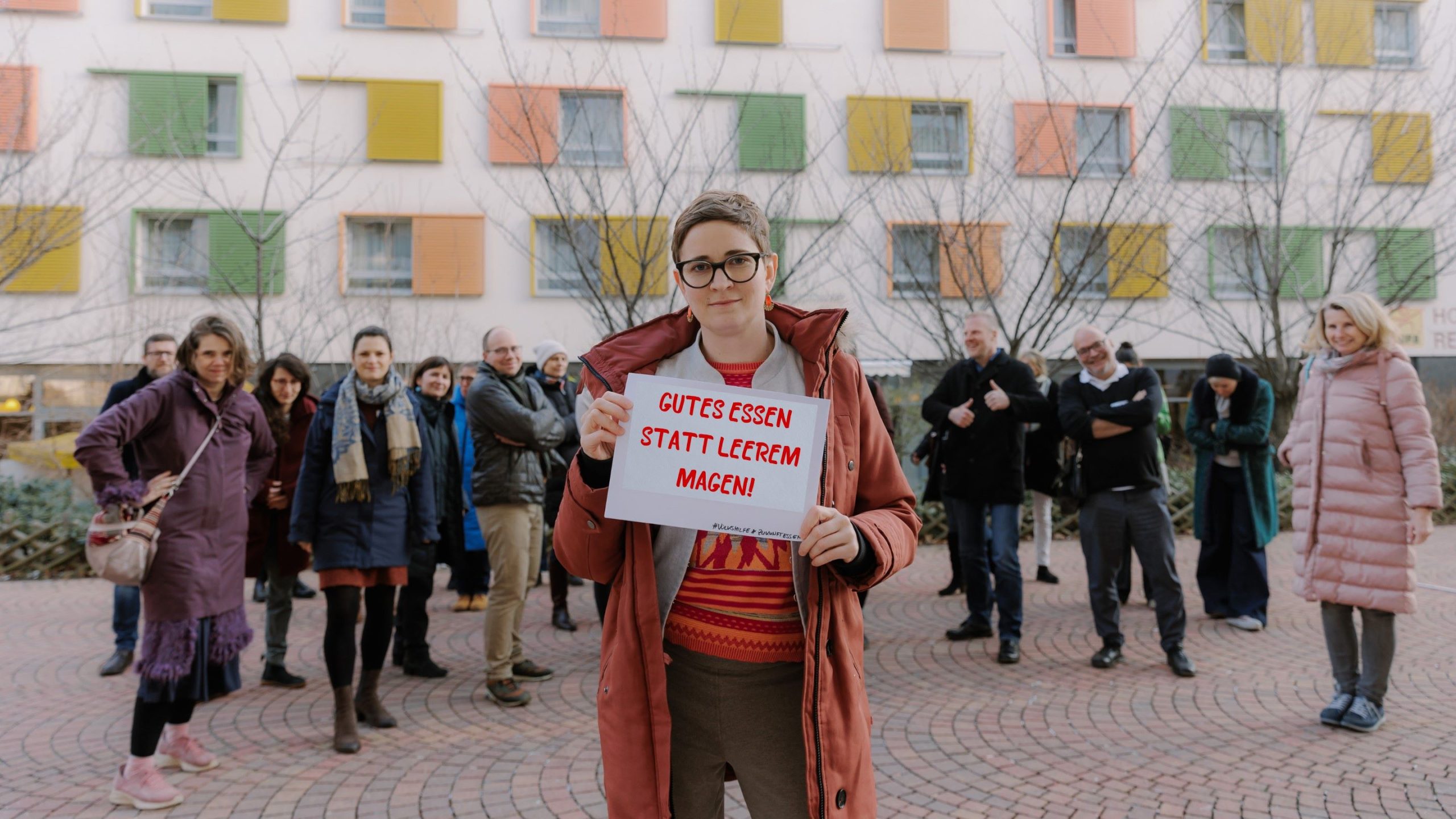 ZUKUNFT ESSEN Obfrau Anna Strobach mit Schild "Gutes Essen statt leerem Magen", im Hintergrund Stakeholder